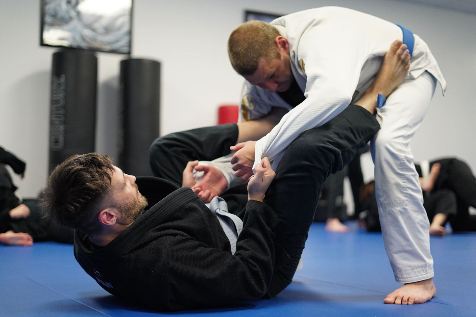 Two adults training Brazilian Jiu-Jitsu on the blue mats