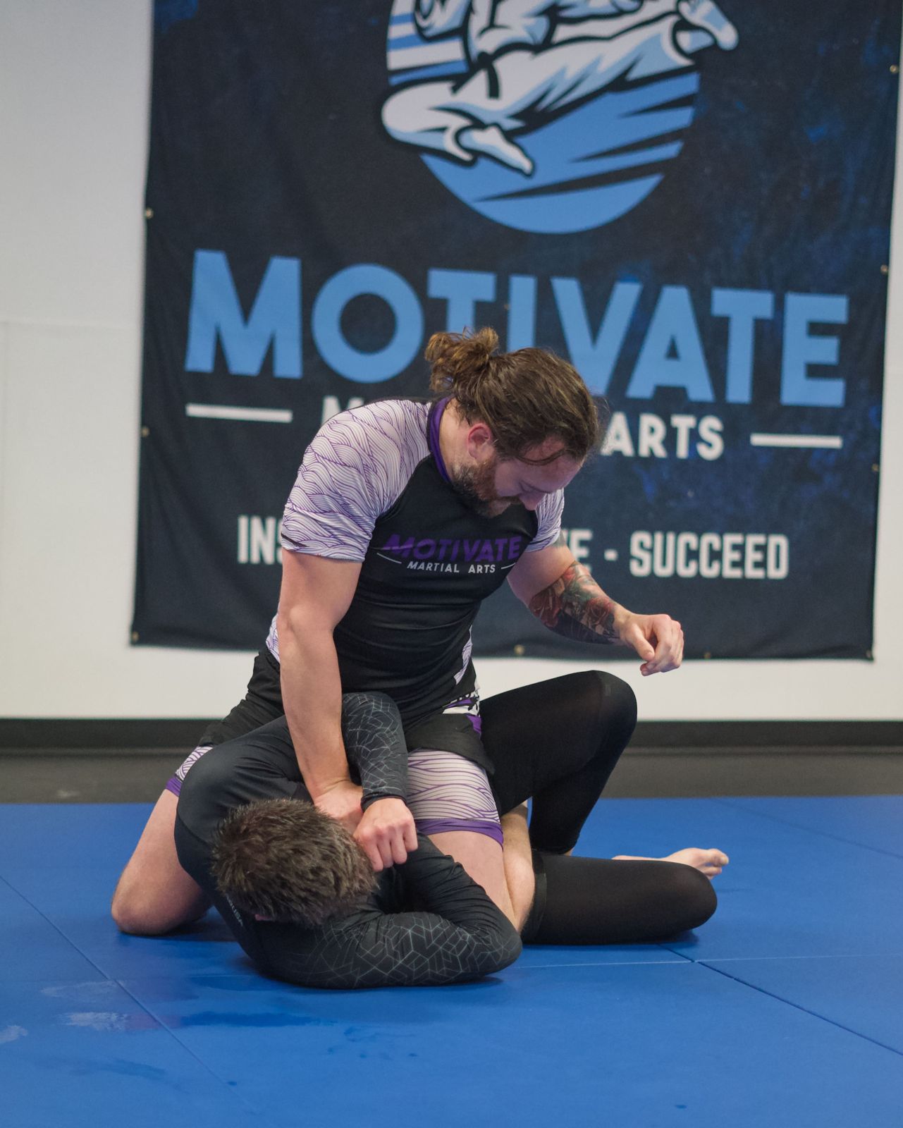 Adult BJJ students training in front of the Motivate banner