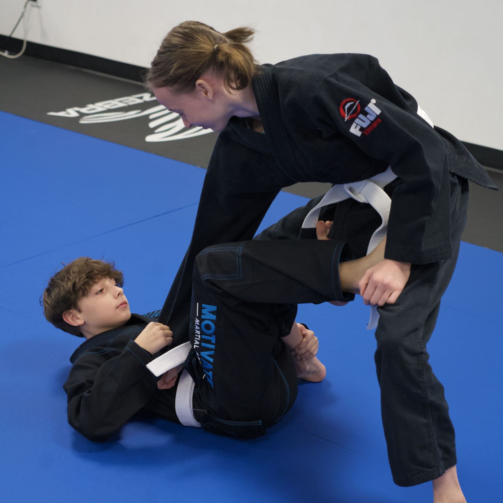 A Juniors BJJ student practicing guard with a partner on the blue mats